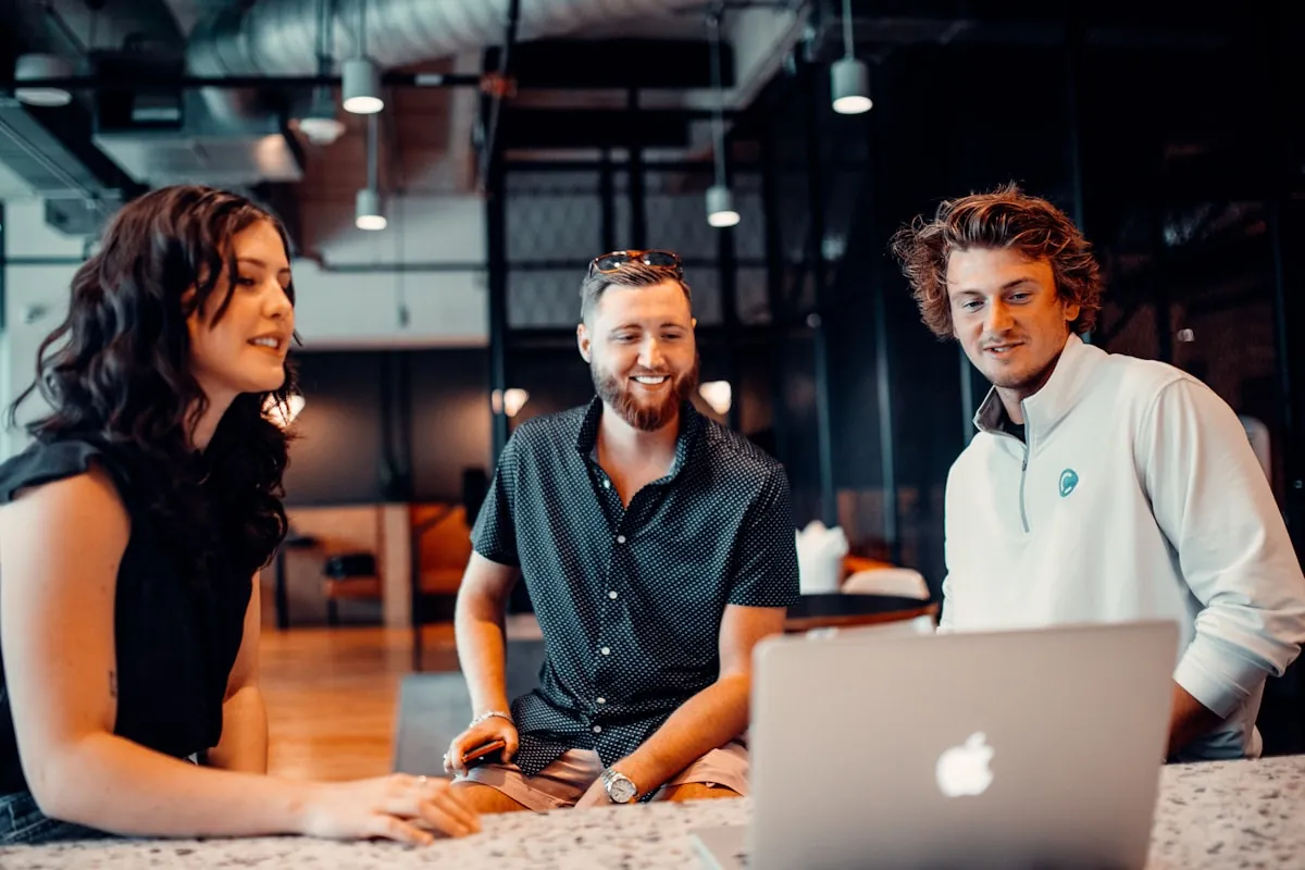 Trois personnes souriantes échangeant autour d'un ordinateur portable dans un bureau moderne